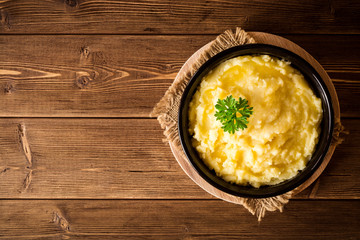 Mashed potatoes with butter and fresh parsley in bowl on rustic wooden table