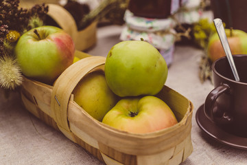 Fresh apples in a wicker basket on a table among dishes, selective focus