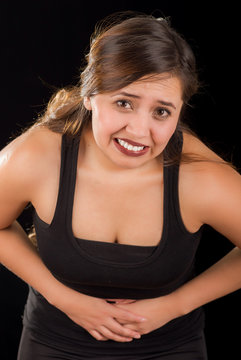 Close up of a beautiful young woman with stomach ache or nausea in a black background