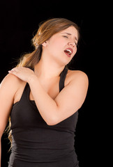 Beautiful young woman suffer from shoulder pain in a black background