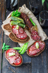 rye sandwich with sausage and tomatoes on wood table