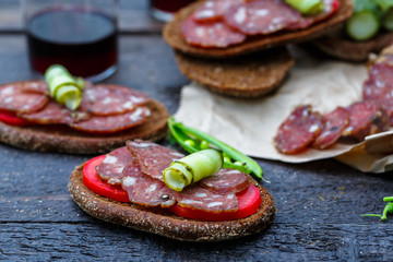 rye sandwich with sausage and tomatoes on wood table.