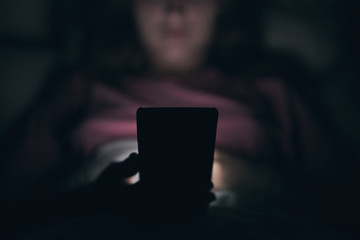 Close-up. A young girl is typing on a smartphone. Lying in bed. Blurred dark background. At night