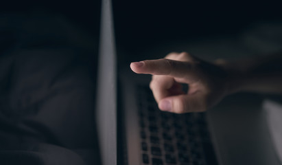 Close-up. A young girl points to a laptop monitor. Hand. Lying in bed. Blurred dark background
