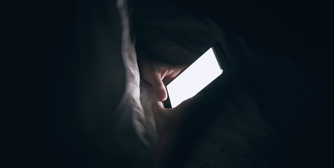 the girl is using the phone. Lying in bed. Dark blurred background