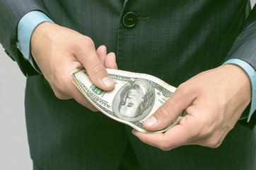 Savings. Pay the debts. The man in the suit holding money dollars in hands in front of him.