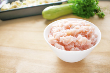 Raw meat. Fresh chicken minced ground-meat in a round white plate on a wooden background. Dietary meat, low-calorie foods. Raw ingredients for vegetable and chicken casserole