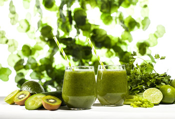 Freshly blended green smoothie in glasses with straws. Green leaves background.