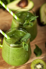 Freshly blended green smoothie in glasses with straws. Wooden background.
