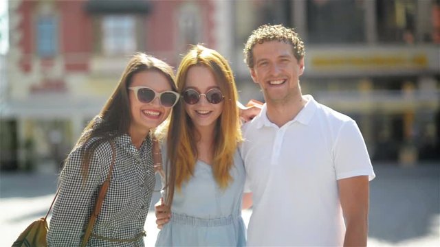 Two Cute Women with Long Hair, Sunglasses and Short Dresses Have Fun Together with Handsome Man in White Shirt in Old City Center During Sunny Summer Day.