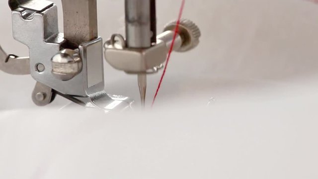 Close-up of the Foot of the Sewing Machine Making the Seam with Red Thread along the White Fabric. Selective Focus is on the Foot.  In the end of video the Fabric Closing the Screen. Copy Space.

