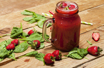 Strawberry smoothie or milkshake in a jar and spinach leaves on wooden background.