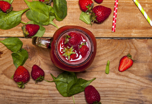 Strawberry smoothie or milkshake in a jar and spinach leaves on wooden background.