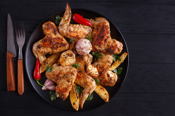 Grilled chicken wings on black plate decorated with garlic and spices, free space for advertisement or text. Cooking concept, meat dishes, homemade food