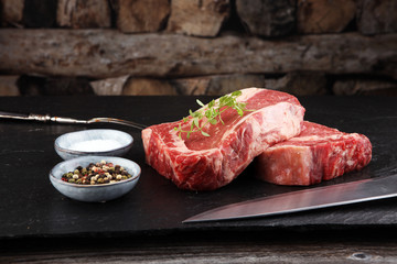 Raw fresh meat Ribeye Steak, seasoning and meat fork on dark background