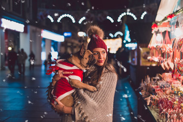 Beautiful brunette woman standing with her adorable French bulldog next to candies selling on street. 