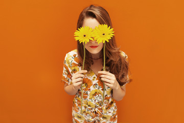 young woman dressing floral pattern jumpsuit in front of an orange wall