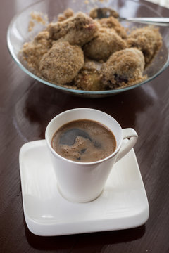 White cup of coffee with plum dumplings in the background