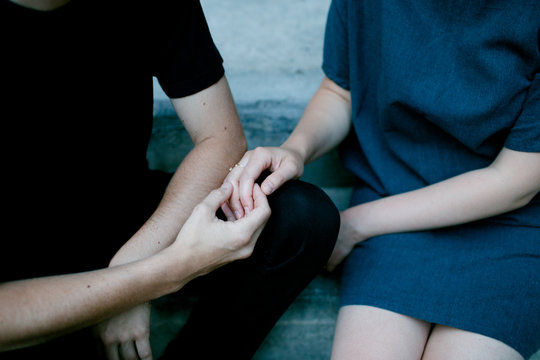 Close up of two women sitting on stoop and holding hands