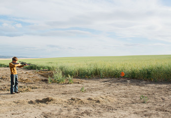 boy aiming bb gun at target in field