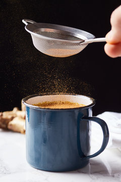 Person powdering turmeric tea with cinnamon