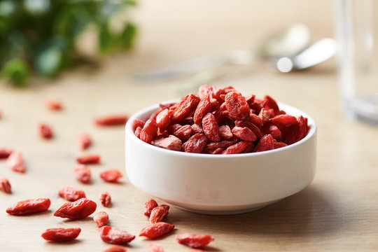 Bowl of goji berries with several scattered on table