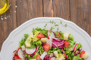 Fresh salad with mixed greens, radish, cheese and tomato in a plate on wooden background. Italian Mediterranean or Greek cuisine. Vegetarian vegan food