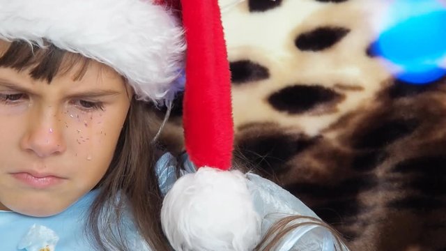Tears of a child in Christmas. A sad little girl in a santa claus hat is crying.