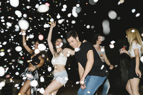 Friends dancing under a confetti rain at night party