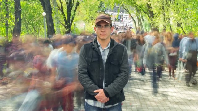 Man standing alone in blurred crowd, on background green trees. Time Lapse, Full HD