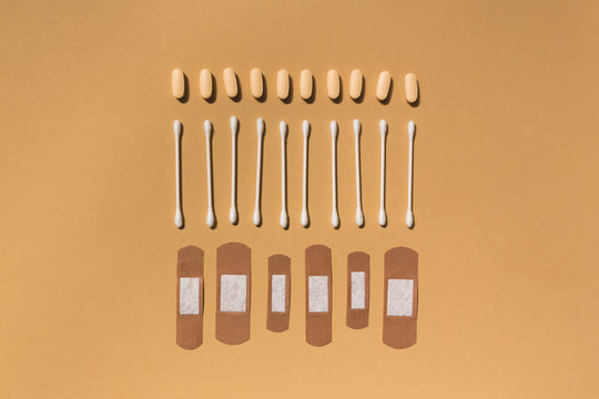Band-aid, cotton swab and pills organized on orange background
