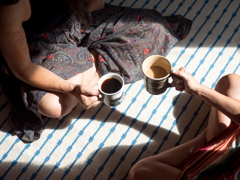 Two young females sitting on floor drinking coffee