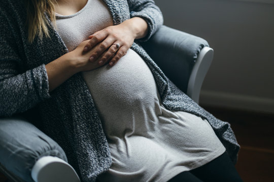 Full Term Pregnant Mother Sitting in Rocking Chair Patiently Waiting For Baby To Arrive