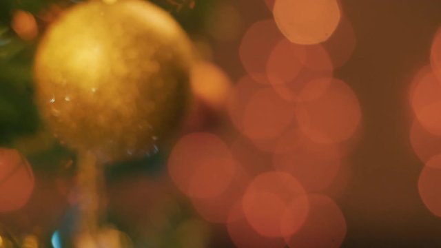 Rack focus shot of a golden Christmas ornament decorating the tree and Christmas lights lens flare.
