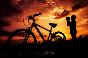 Obraz premium Silhouette of boy and bicycle on sunset background