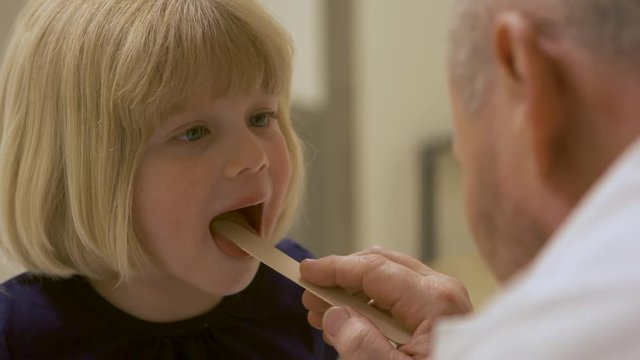 Close up of doctor using tongue depressor to examine child's throat.