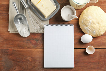 Notebook and raw dough with ingredients on kitchen table. Cooking classes concept