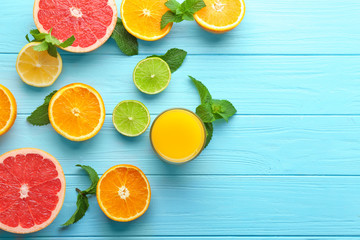 Composition with glass of fresh juice and citrus fruits on color wooden background