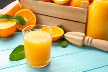 Glass of fresh juice and oranges in box on wooden table