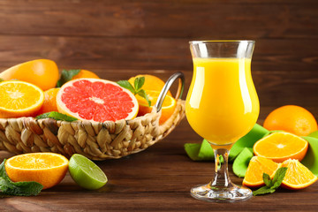 Composition with glass of fresh juice and citrus fruits in wicker basket on wooden table
