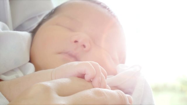Close-up of parents hands holding newborn and baby sleep on her arms. Concept of happy family desire in no noisy home and carefree