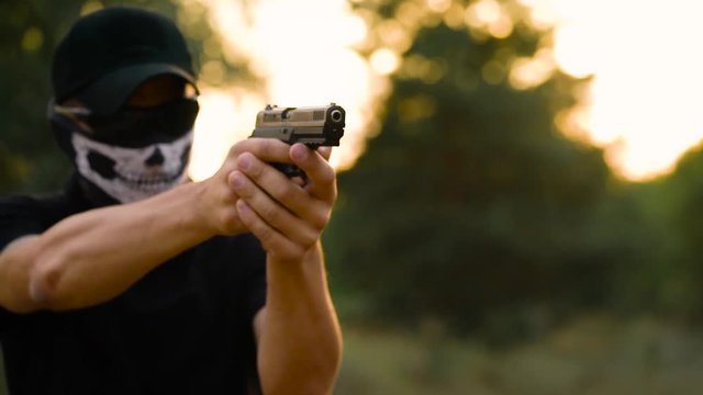 Man with the face closed with a handkerchief and sunglasses getting ready to shoot a gun, close up. Slow motion