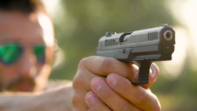 Young man is shooting from a gun, close up. Slow motion