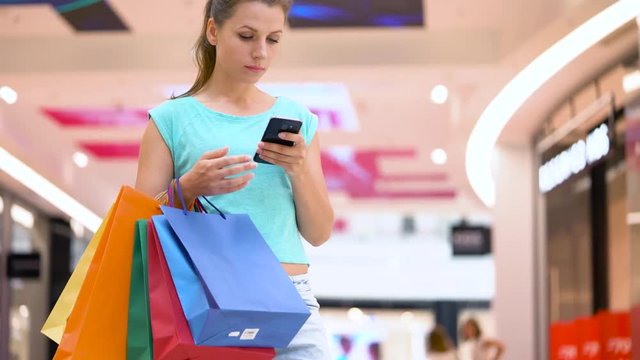 Woman with paper bags using smartphone in a shopping center