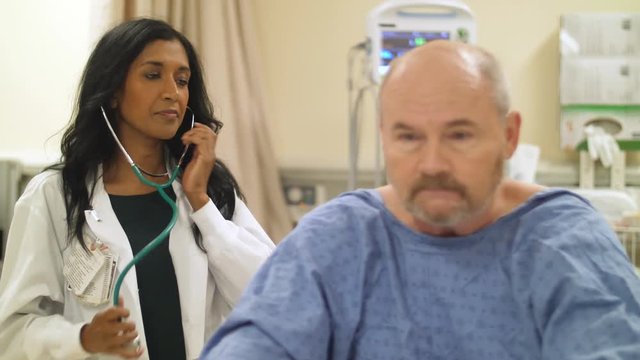 Female doctor listens to patient's heart with a stethoscope bedside in hospital.