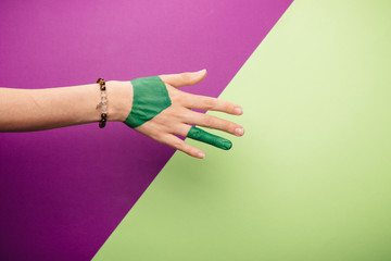 one woman hand, Caucasian painted green hand skin, green purple magenta background, jewelery bracelet