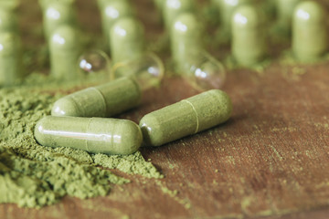 Herbal medicine in capsules with green powder herbs on wooden table