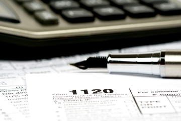 1120 tax forms closeup with calculator and ink pen