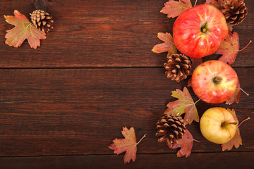 Autumn concept, fallen red-yellow currant leaves with apples and pine cones on a wooden table. Thanksgiving Day.
