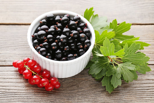 Black currants in bowl with leafs on grey wooden table